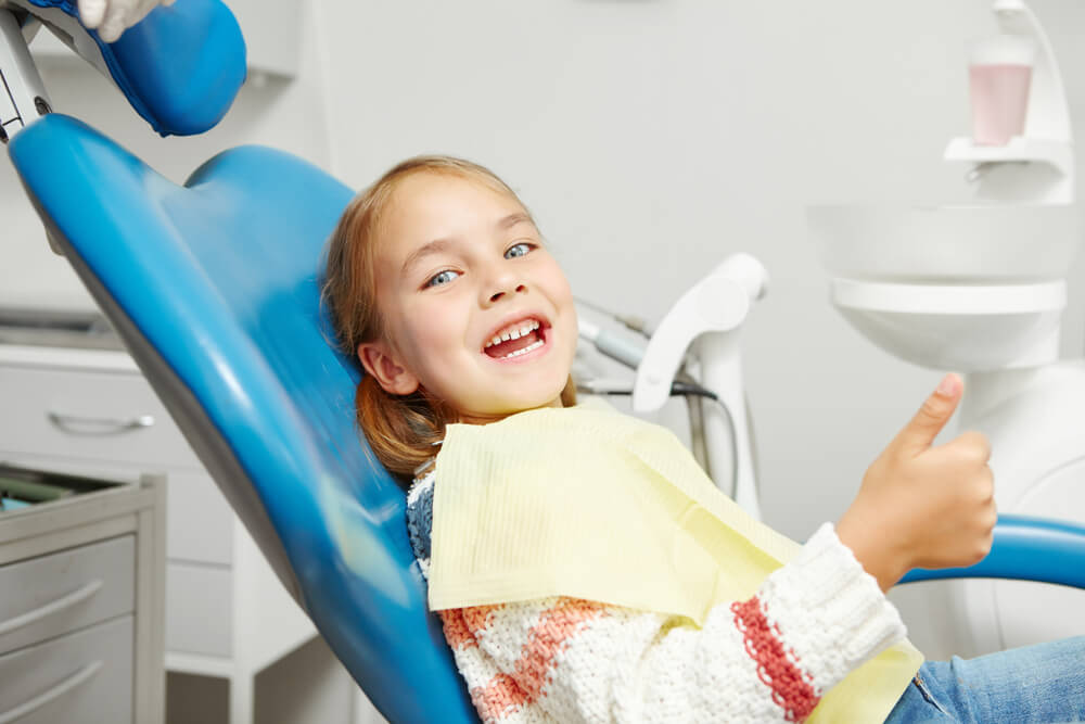 Young girl giving a thumbs up while sitting in a dental chair